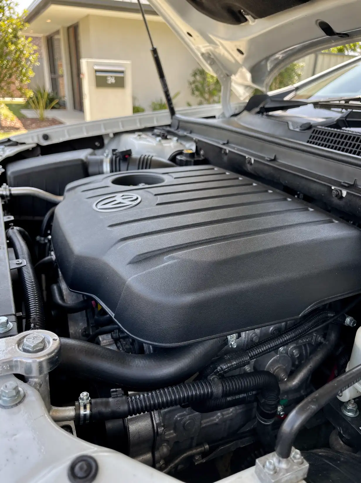 Freshly detailed matte-black engine cover with clean hoses and bright fittings, Perth car detailing.